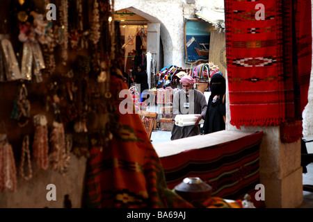 A Muslim woman shops in Souq Waqif Doha Qatar while a porter assists her with her goods A woman works yarn in the background Stock Photo