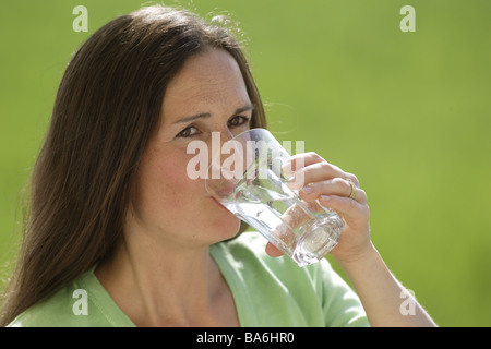 Woman long-haired brunette glass water drinks outside portrait 30-40 years mineral water tumbler background green nutrition Stock Photo