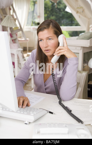 Studies desk woman works computers telephones seriously semi-portrait apartment office people 40-50 years independent freelance Stock Photo