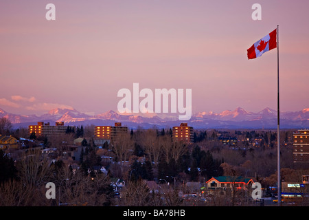 Canadian flag flying from a flag pole in the city of Calgary with the Canadian Rocky Mountains of Banff National Park. Stock Photo
