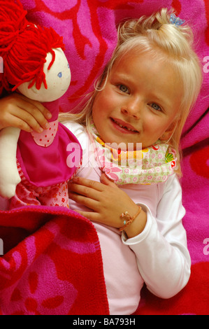Girls smiles doll cuddles lies portrait series people 5 years child-portrait child toddler blond gaze camera scarf childhood