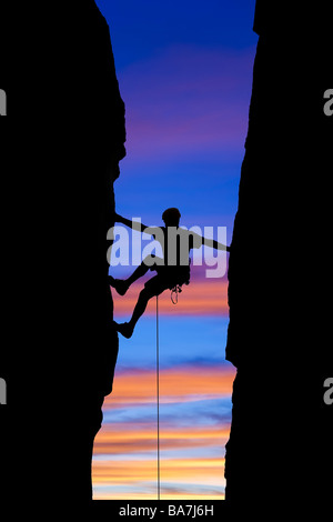Rock climber silhouetted as he reaches across a gap. Stock Photo