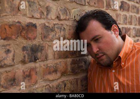Sad man leaning against a brick wall Stock Photo
