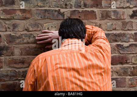 Man in orange stripy shirt hiding face against the rick wall Stock Photo