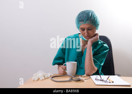 Tired doctor sat in office drinking coffee Stock Photo