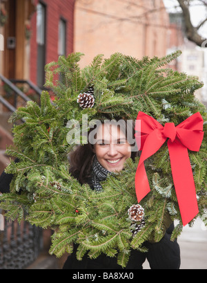 Woman carrying Christmas wreath on urban street Stock Photo