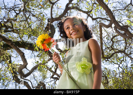 African American girl in dress holding flowers underneath tree Stock Photo