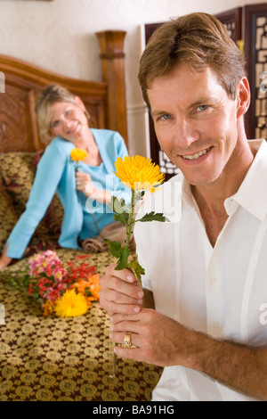 Portrait of happy couple sitting on bed with flowers Stock Photo