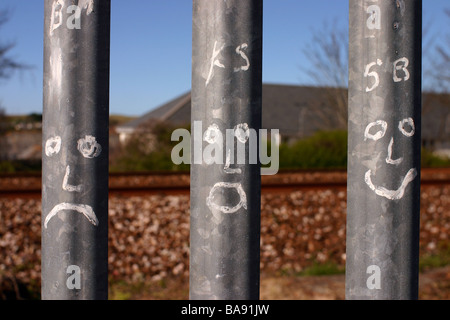 Happy and sad faces painted on metal fence by railway line UK Stock Photo