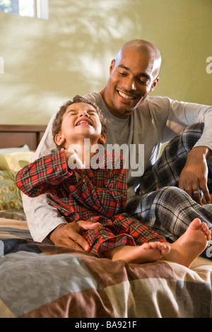 African-American father and son sitting on bed in pajamas