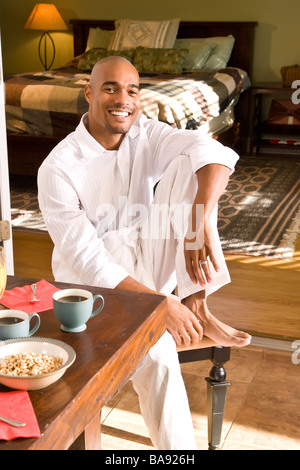 African-American man sitting at breakfast table with leg up Stock Photo