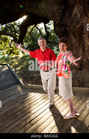 Portrait of middle-aged couple dancing on boardwalk under tree Stock Photo