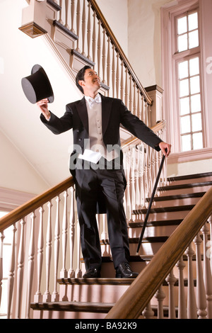 Asian man in tuxedo standing on stairs with top hat and cane Stock Photo