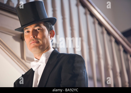 Asian man in tuxedo standing on stairs with top hat Stock Photo