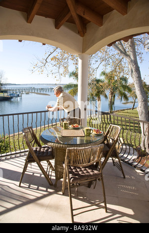 Portrait of senior man standing on veranda of house, looking at view Stock Photo