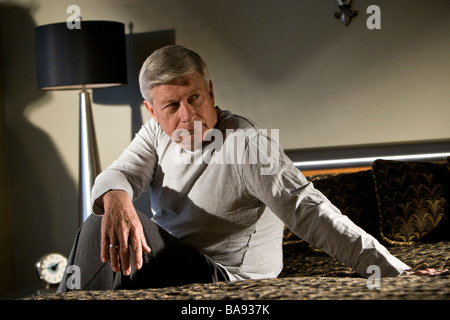 Portrait of senior man sitting on bed looking away Stock Photo