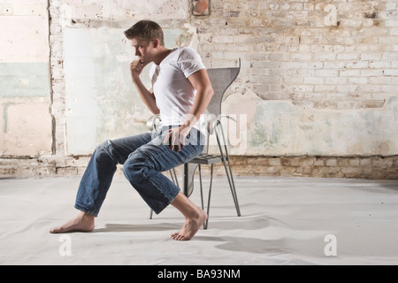 Young man sitting in chair in warehouse Stock Photo