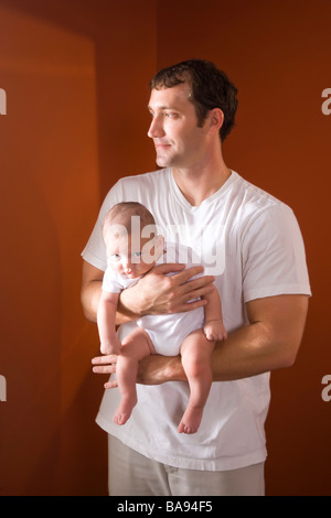 Portrait of father holding 3 month old baby at home looking out window Stock Photo