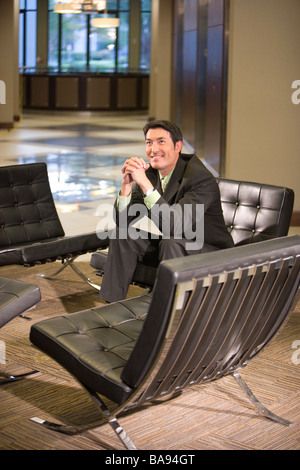 Confident Asian businessman sitting in modern office lobby Stock Photo