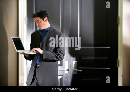 Asian businessman standing in office hallway using laptop Stock Photo