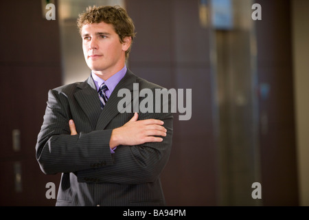 Portrait of young businessman standing in lobby, arms folded Stock Photo