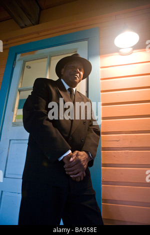 Senior African American man in suit and hat leaning against porch door at night Stock Photo