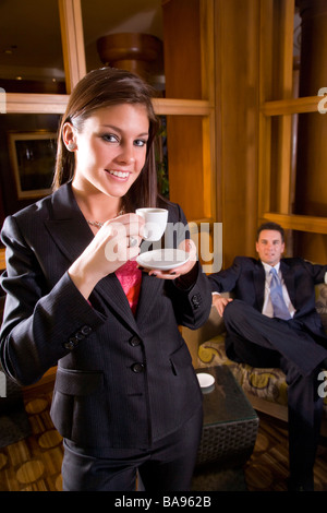 Businesswoman drinking coffee with businessman in background Stock Photo