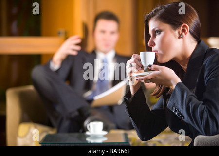 Beautiful woman sipping cup of coffee with businessman in background Stock Photo