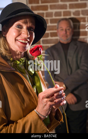 Middle-aged woman holding red rose, man in background Stock Photo