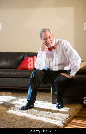 Middle-aged man in bowtie sitting on living room sofa Stock Photo