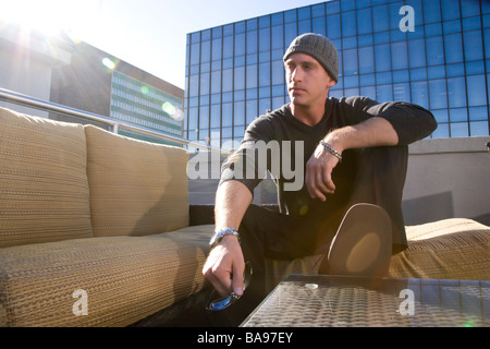 Young thoughtful man sitting on rooftop of downtown condo in city Stock Photo