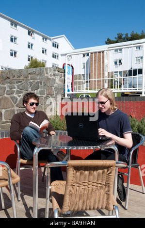 Two male students at Aberystwyth university using a laptop computer outdoors accessing campus wireless network sunny afternoon Stock Photo
