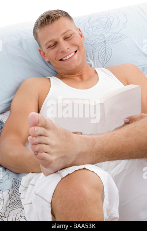 smiling handsome male reading book in bed Stock Photo