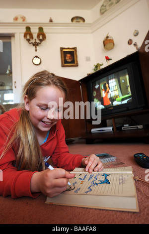 Young 9 yr old girl watches television as she draws in her sketchbook Stock Photo