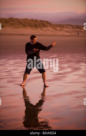 One mid adult man practices Taekwondo on the beach at sunset in Morro Bay, California. Stock Photo