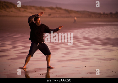 One mid adult man practices Taekwondo on the beach at sunset in Morro Bay, California. Stock Photo