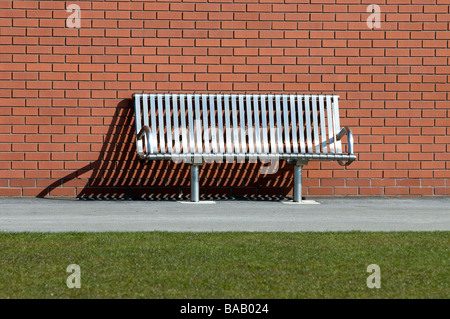 Stainless steel bench against red brick wall with harsh shadows Stock Photo