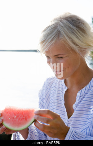 A woman eating a watermelon by the sea in the archipelago of Stockholm, Sweden. Stock Photo