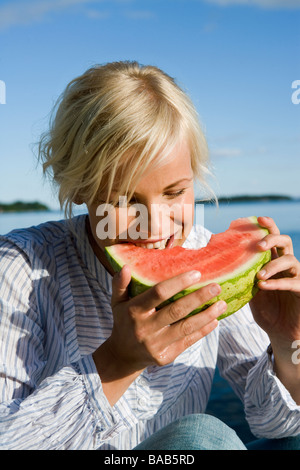 A woman eating a watermelon by the sea in the archipelago of Stockholm, Sweden. Stock Photo