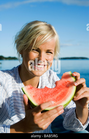 A woman eating a watermelon by the sea in the archipelago of Stockholm, Sweden. Stock Photo