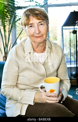 Senior woman sitting and smiling happily with cup of tea Stock Photo