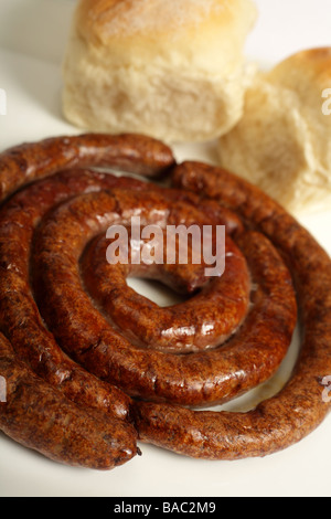 A plate of grilled boerewors South African farmers sausage in its traditional spiral with bread rolls in the background Stock Photo