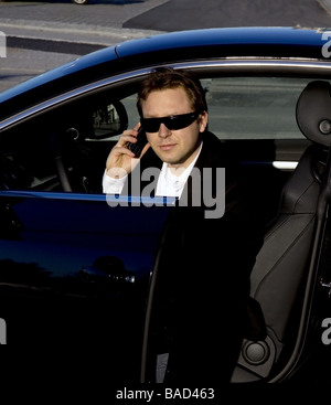 A stylish business executive in a German luxury car. He is talking on his cell phone while getting out of the car. Stock Photo