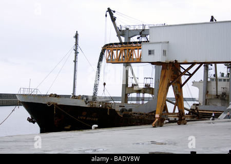 'Lien Shuan' general cargo ship being loaded with gravel from conveyor belt at bulk cargo terminal area, warehouse zone, Hualien Port, Taiwan Stock Photo