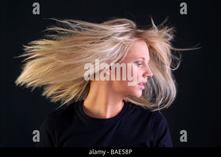 A beautful young woman with long blonde hairstyle turning her head so her hair flows black background Stock Photo