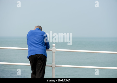 A middle aged man wearing a blue jacket leaning on the railings on the promenade at Aberystwyth wales UK, summer afternoon Stock Photo