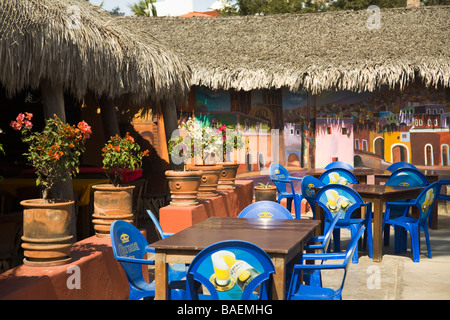 MEXICO La Playita Tables and chairs in outdoor dining area for Tommy s Barefoot cantina restaurant painted mural on wall Stock Photo