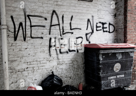 graffiti on white brick wall in a run down alley surrounded by rubbish, stating 'we all need help' Stock Photo