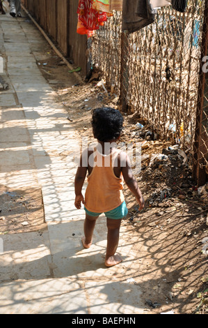 A Small Child Walking alone in the sunshine in a settlement in the Colaba area of South Mumbai, India Stock Photo