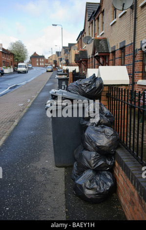 Plastic bags piled up beside an overflowing black bin ready to be collected. Stock Photo
